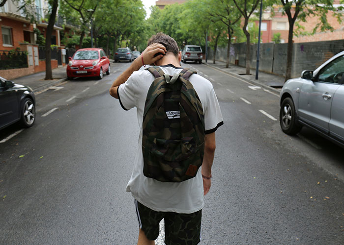 Person with camo backpack walking on a quiet street, representing the concept of overheard public conversations.