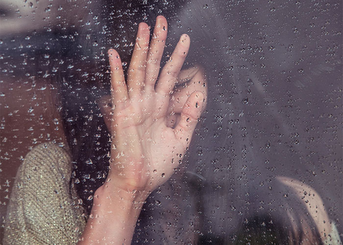 A hand pressed against a rain-covered window, evoking the feeling of overhearing things in public spaces.