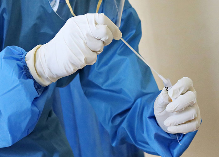 Medical professional in PPE handling a swab, illustrating public health precautions.