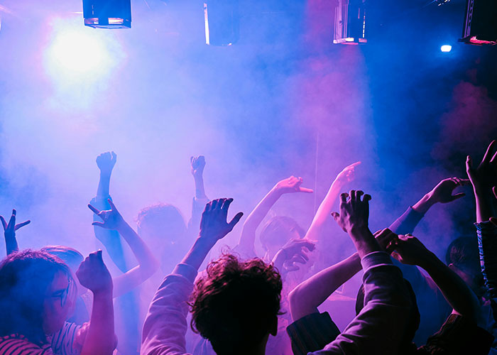 People dancing at a concert, colorful lights and fog create a vibrant setting, illustrating insane public moments.