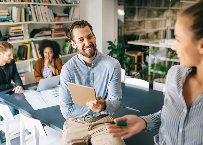 Smiling man holding a tablet in a casual meeting, discussing things overheard in public.