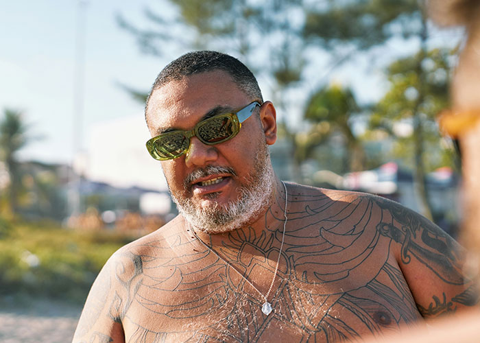 Man with sunglasses and tattoos at the beach, representing overheard public conversations.