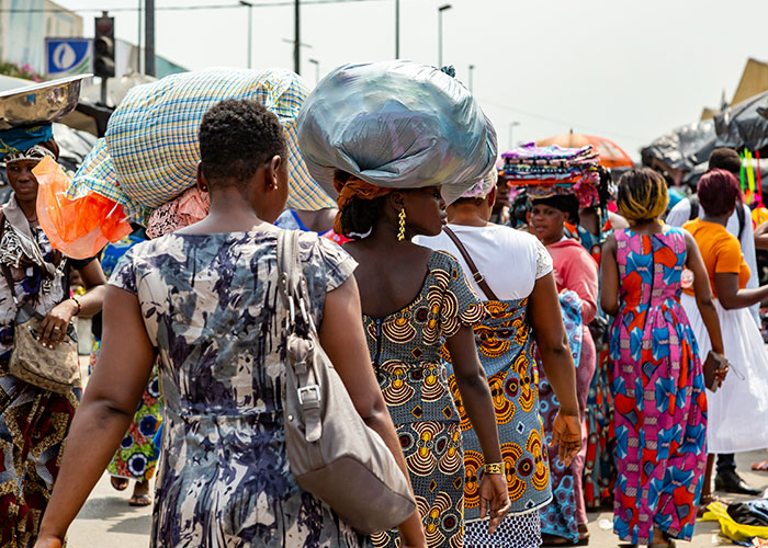 People carrying goods on their heads in a bustling market street, showcasing vibrant public scene.