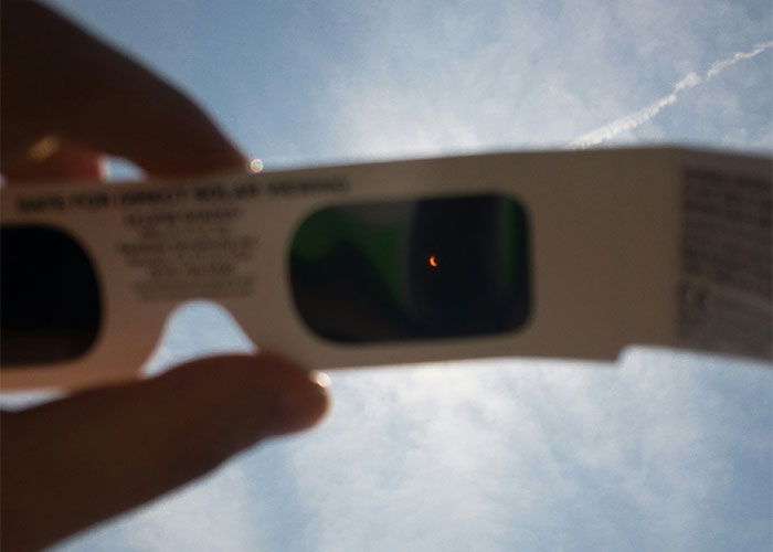 Viewing the sky through eclipse glasses, illustrating public experiences.