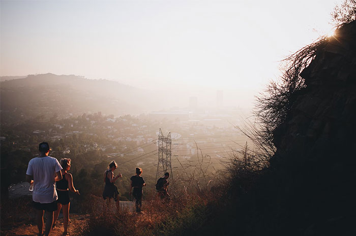 People hiking down a scenic trail overlooking a city, with sunlight casting a warm glow over the landscape.