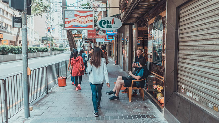 People walking on a busy city sidewalk, while others sit outside a shop, capturing the essence of intuition in everyday life.