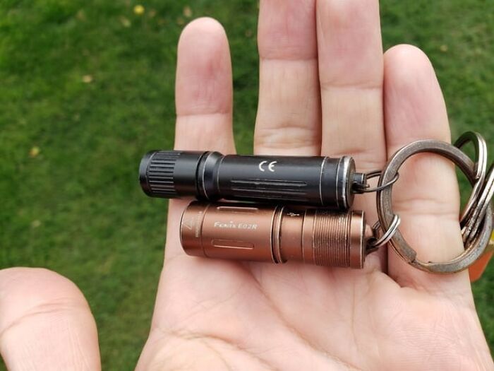 Hand holding keychain with sentimental items, including small flashlights.