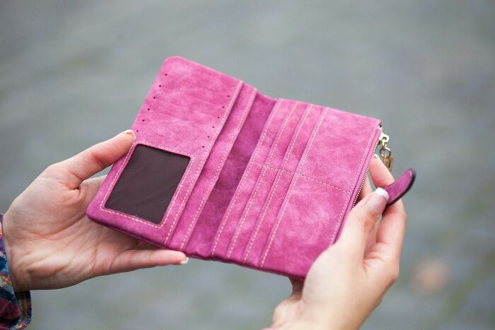 Empty pink wallet, held open by hands, symbolizing sentimental items people carry despite being rather useless.