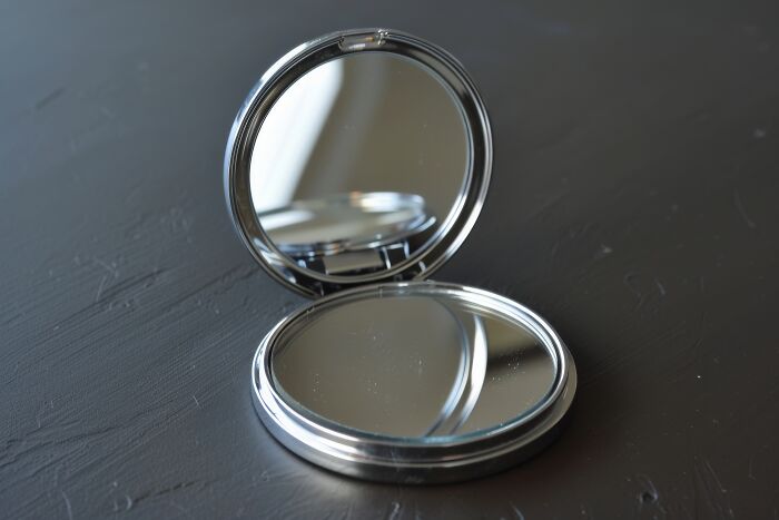 Compact mirror open on a dark surface, maybe carried for sentimental reasons but rather useless.