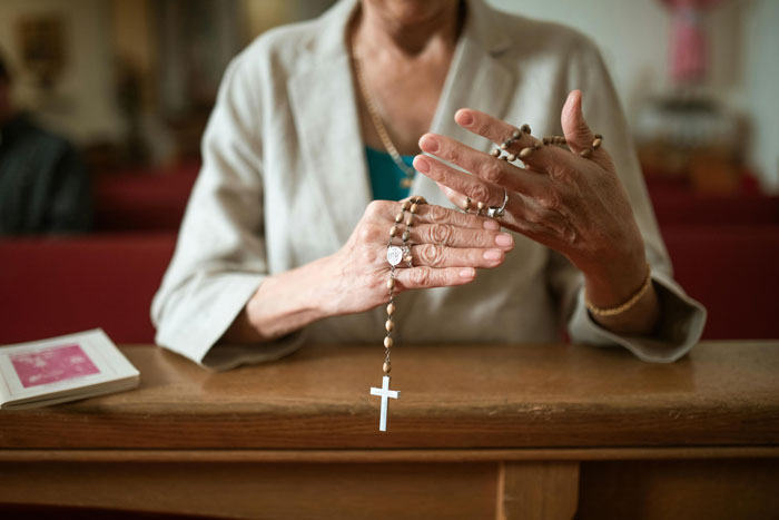 Religious MIL holding rosary, seated in church setting, with focus on hands and cross. Religious MIL holding rosary, seated in church setting, with focus on hands and cross.
