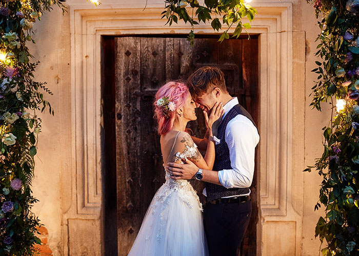 Bride and groom embracing in floral archway, smiling, during a wedding moment. Bride and groom embracing in floral archway, smiling, during a wedding moment.