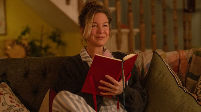 Smiling woman from "Bridget Jones: Mad About the Boy" on a couch holding a red book, related to anticipated movies of 2025.