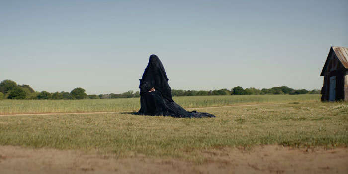 A mysterious figure from "The Woman in the Yard" in a black cloak sits in an open field, related to anticipated movies of 2025.