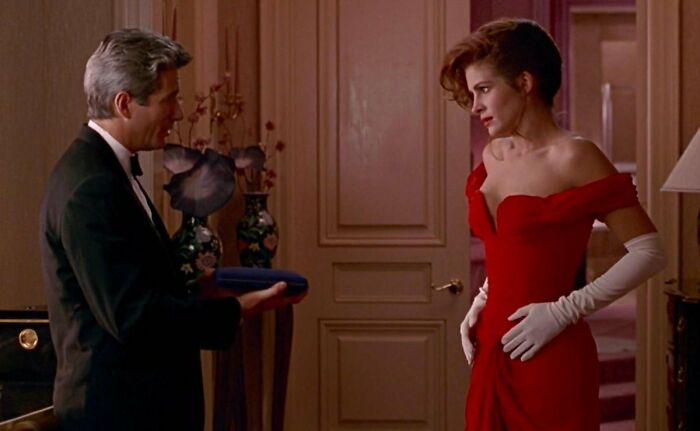 Man in a tuxedo presenting a jewelry box to a woman in a red dress and white gloves; iconic famous movie props moment.