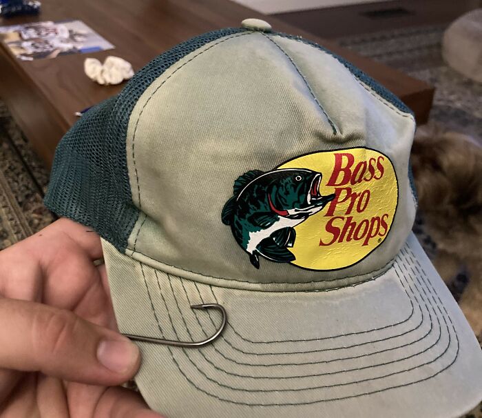 A person holding a fishing cap labeled "Bass Pro Shops." Recent fashion trends people hate include similar accessories.
