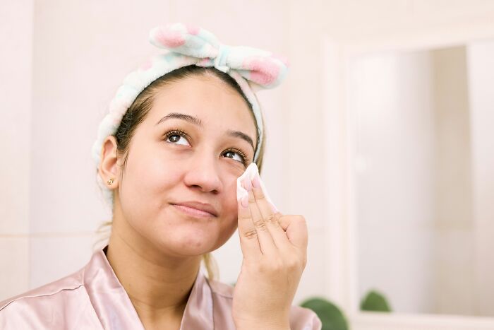 Woman with a headband using a cotton pad on her face, reflecting on offensive comments.