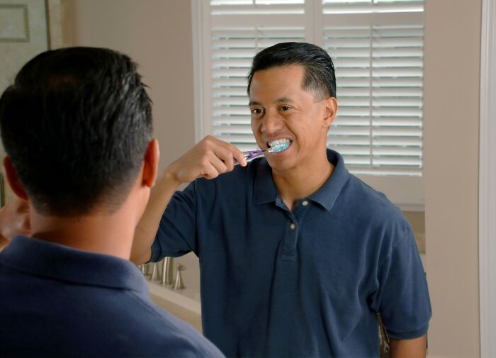 Man brushing teeth in front of a mirror, wearing a navy blue polo shirt, illustrating unrealistic movie moments.