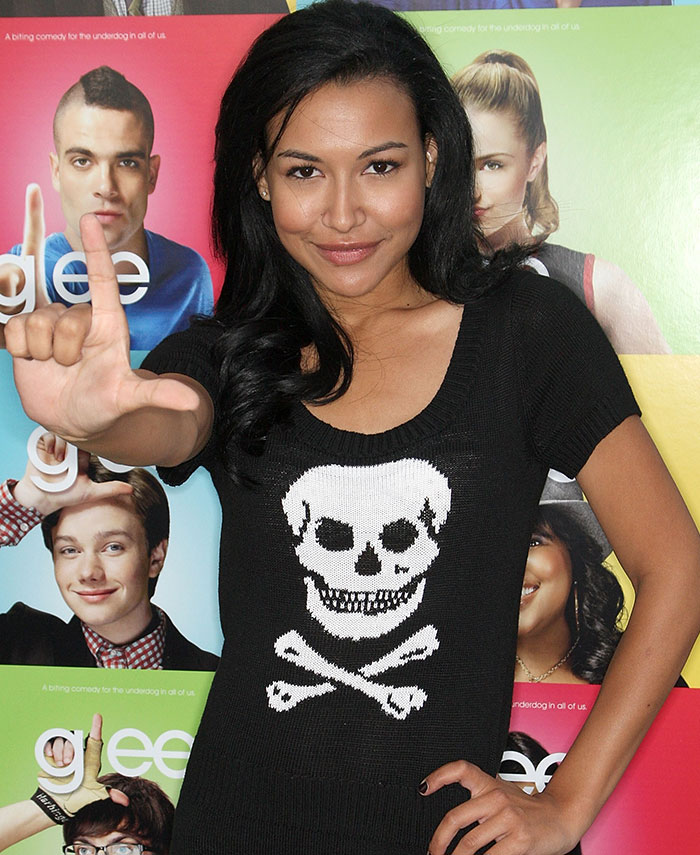 "Person in skull sweater posing in front of a colorful TV show poster backdrop."