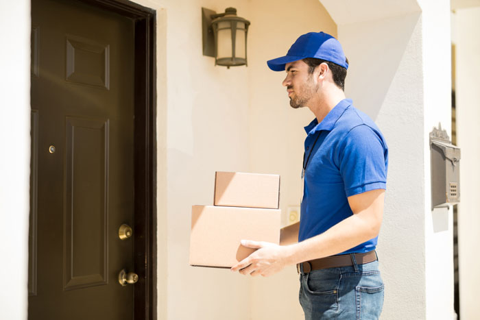 Delivery person holding packages at a front door, wearing a blue cap and shirt, part of neighborhood loans context.
