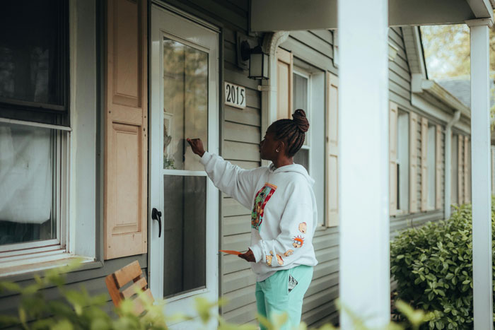 Woman knocking on a neighbor's door, wearing a white hoodie and green pants, in a suburban setting. Woman knocking on a neighbor's door, wearing a white hoodie and green pants, in a suburban setting.