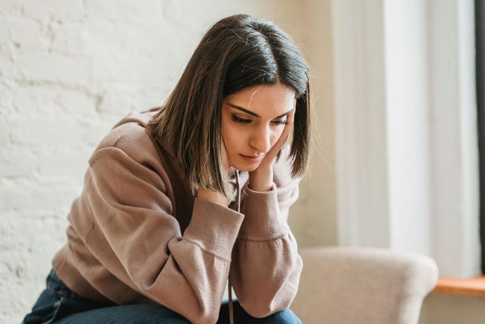 Woman in a beige sweater looking thoughtful, seated on a chair with a neutral background. Woman in a beige sweater looking thoughtful, seated on a chair with a neutral background.