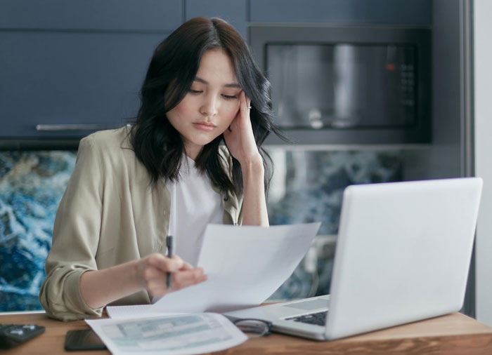 Woman reviews documents at a desk with a laptop, concerned about neighbor hounding for money. Woman reviews documents at a desk with a laptop, concerned about neighbor hounding for money.
