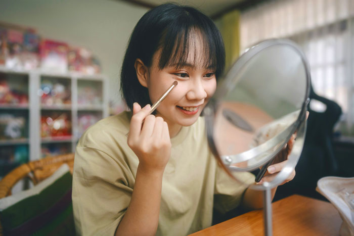 Woman applying makeup with a brush in front of a mirror at home. Woman applying makeup with a brush in front of a mirror at home.