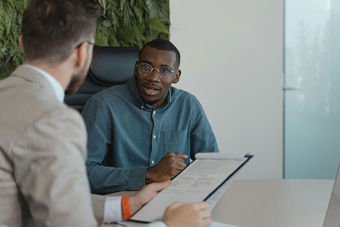 Man in a blue shirt discusses with another man holding a document, illustrating HR challenges in an office setting. Man in a blue shirt discusses with another man holding a document, illustrating HR challenges in an office setting.
