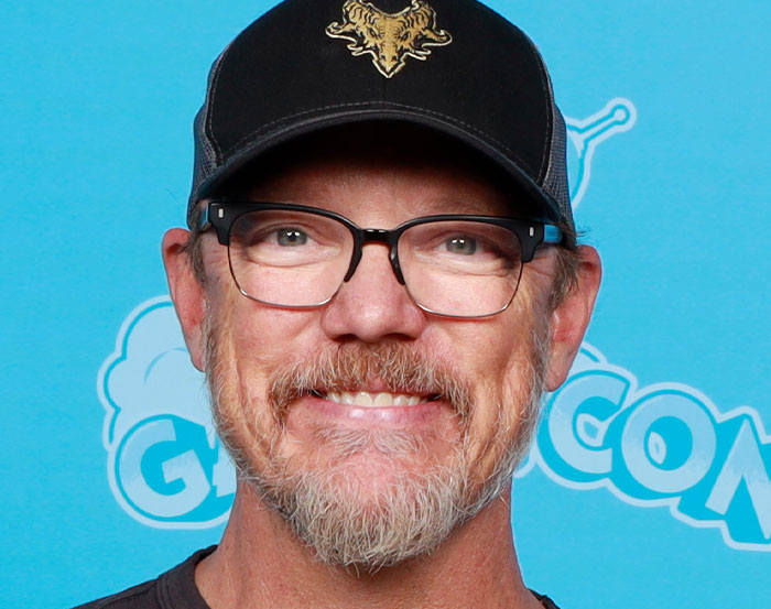Man with glasses and a cap smiling at a comic event.