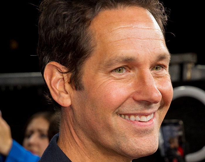 Smiling Paul Rudd at an event, warmly interacting with fans in the background.