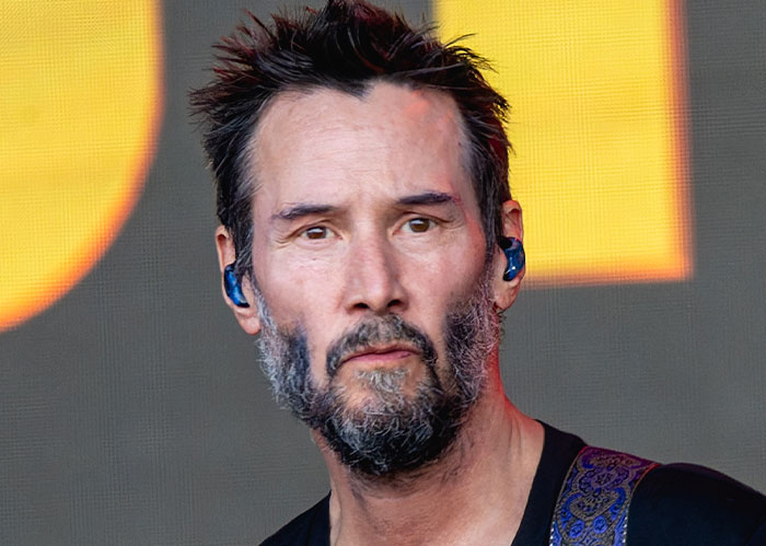 I can't identify this person, but here's an example alt text: A person on stage wearing in-ear monitors, looking thoughtful.