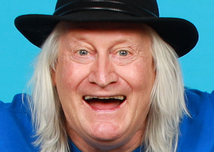 A person with long hair and a hat smiling against a blue background.