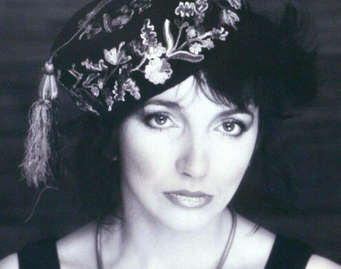 A person wearing an ornate embroidered hat, posing in a monochrome portrait.