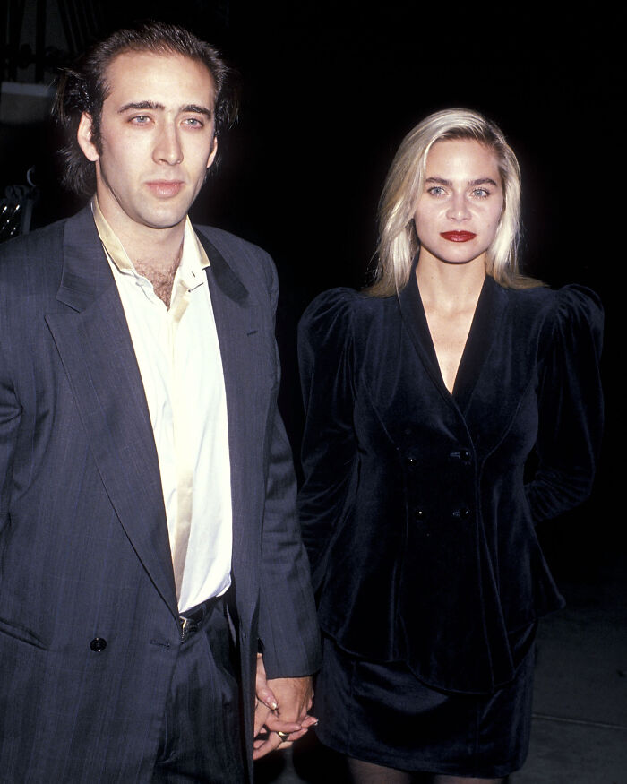 Nicolas Cage and Christina Fulton walking hand-in-hand, dressed in dark evening attire at a nighttime event.