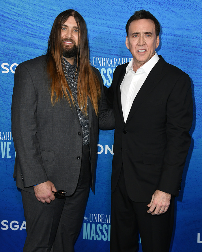 Nicolas Cage and Weston Coppola Cage in suits at a blue-themed event, posing for a photo.
