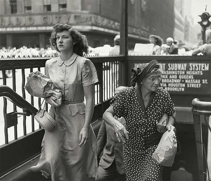 Women exiting a vintage subway entrance, carrying grocery bags, in a scene from more than a hundred years ago.