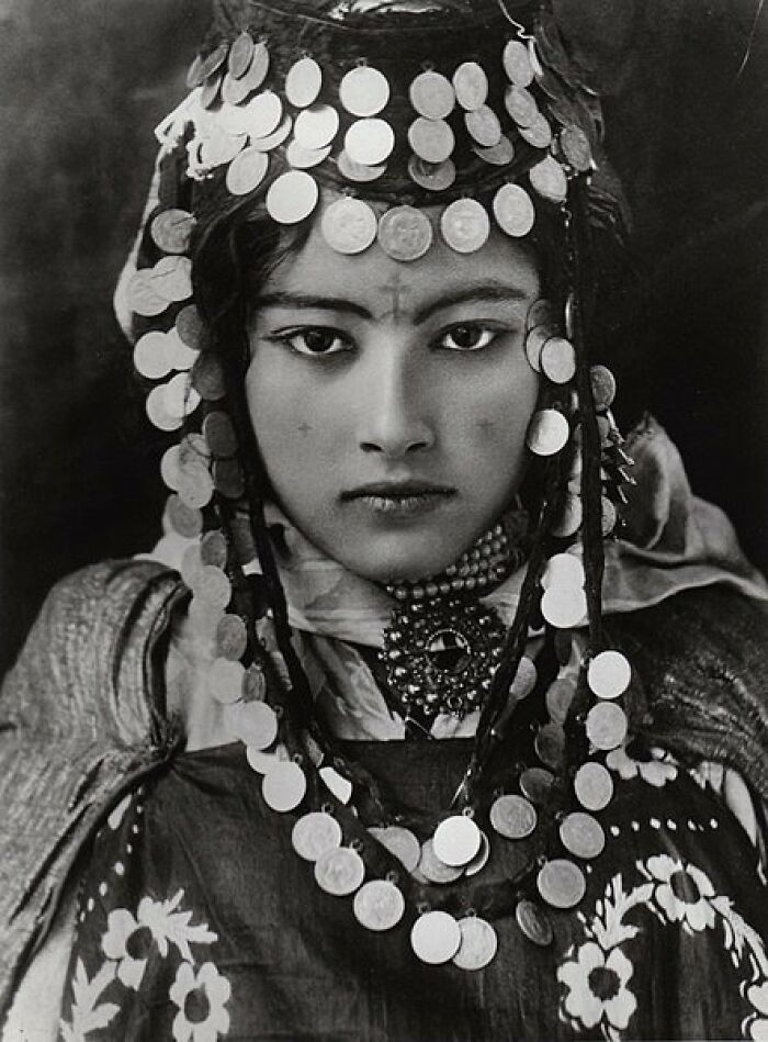 A woman adorned in traditional coin jewelry, showcasing historical attire from over a hundred years ago.