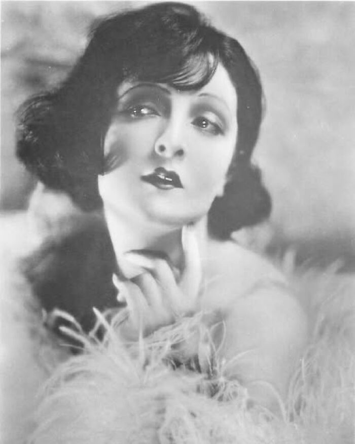 Vintage portrait of a woman with dark hair and feathered attire, representing photos from a hundred years ago.