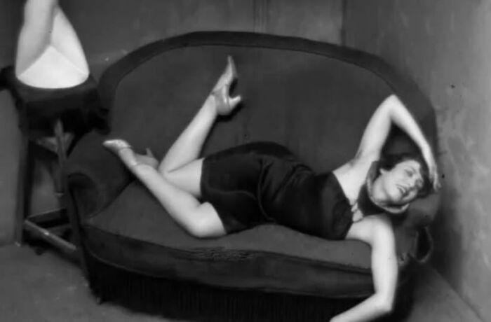 Woman in vintage attire posing on a vintage couch, evoking timeless resonance and historical charm.