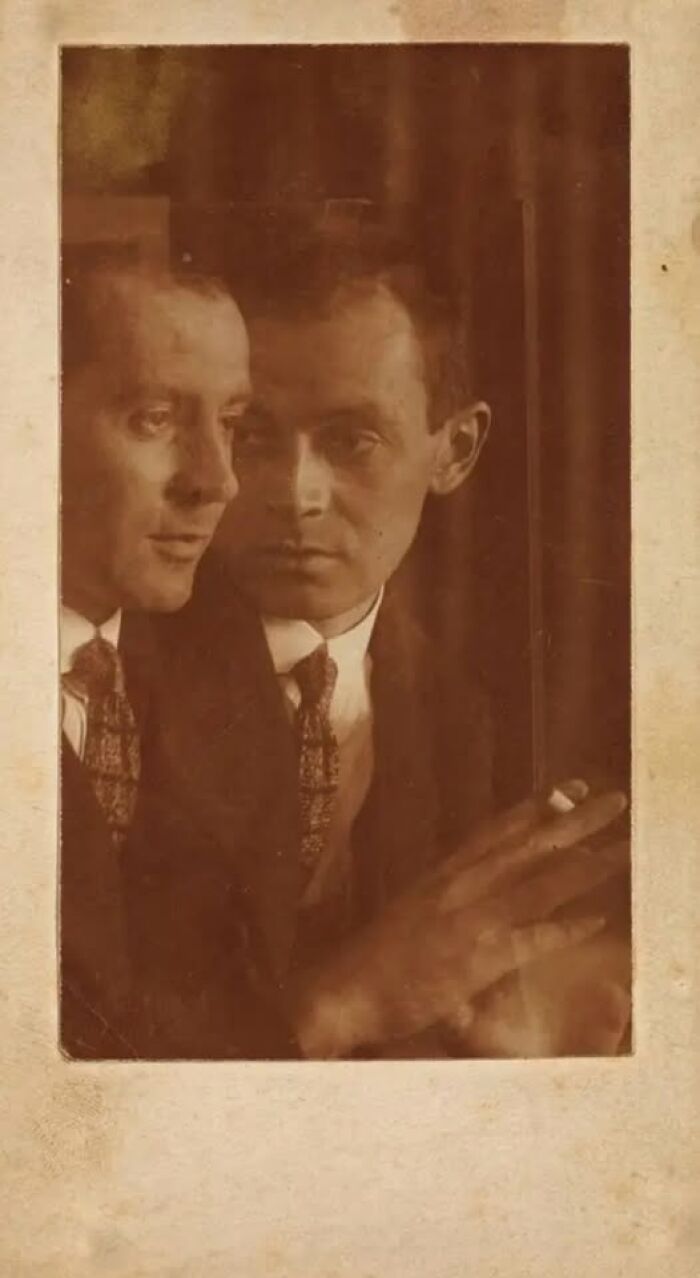 Sepia-toned photo of a man dressed in early 1900s attire beside his reflection, capturing a historical moment.