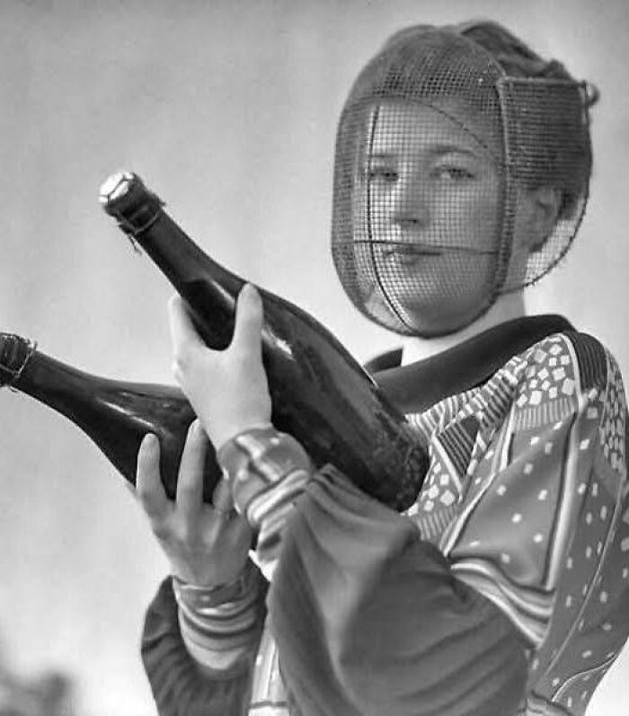 A woman from the early 20th century wearing a mesh mask, holding two large bottles, illustrating historical resonance.