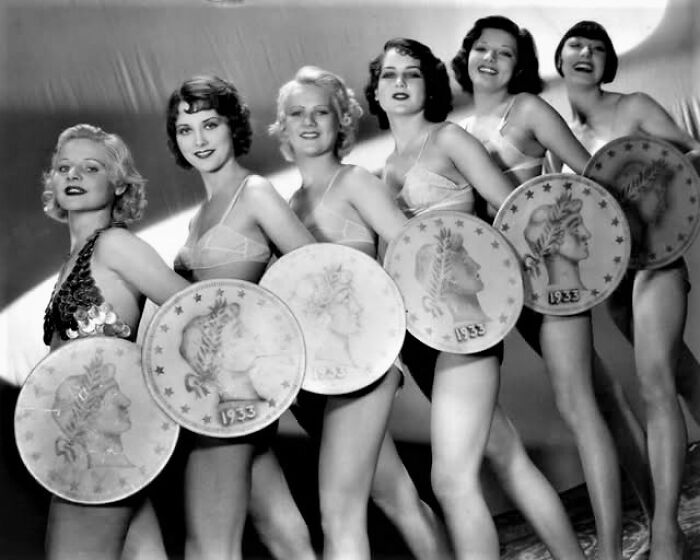 Women from the past posing with large coin props, representing lasting cultural resonances over the century.