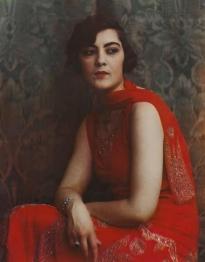 Woman in a vintage red dress from over a hundred years ago, posing against a patterned backdrop.