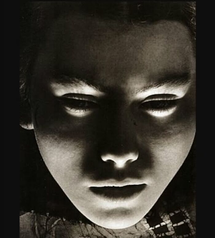 Vintage photograph of a face, dramatically lit from below, creating an eerie and timeless effect.