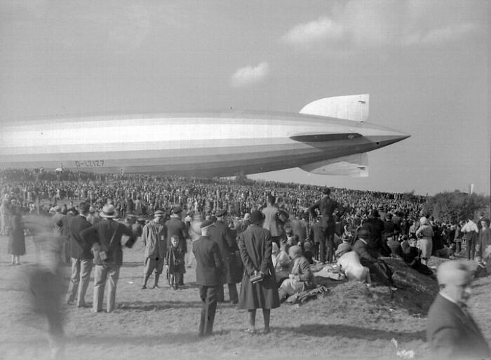 Crowd gathered near an airship from a hundred years ago, illustrating historical resonance.