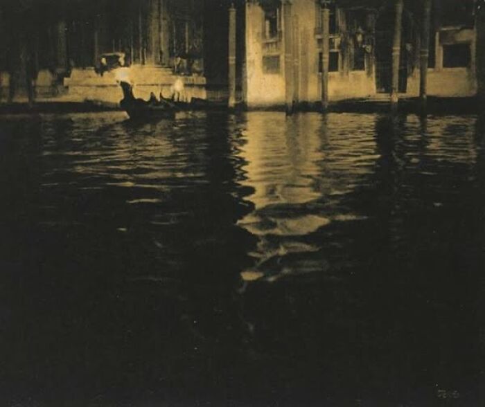Historical photo of a gondola on a dimly lit canal, evokes timeless resonance with reflections on the water.