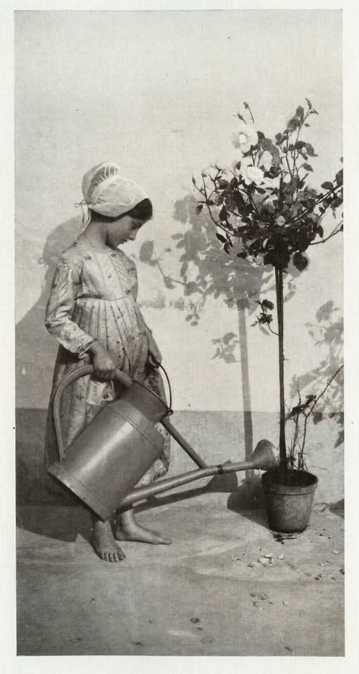 Young girl watering a potted plant with a vintage watering can, wearing a bonnet and dress, historic photo over 100 years old.