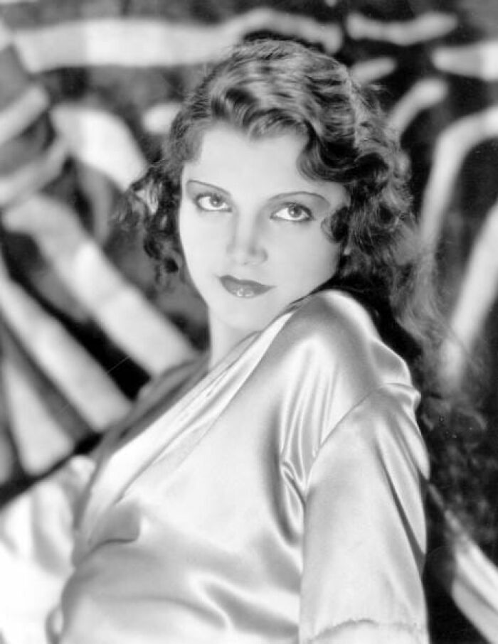 Vintage portrait of a woman from more than a hundred years ago, wearing a shiny blouse with curled hair, gazing intensely.