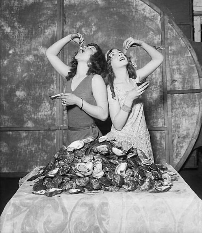 Two women enjoying oysters at a large table, a moment from over a hundred years ago that resonates today.