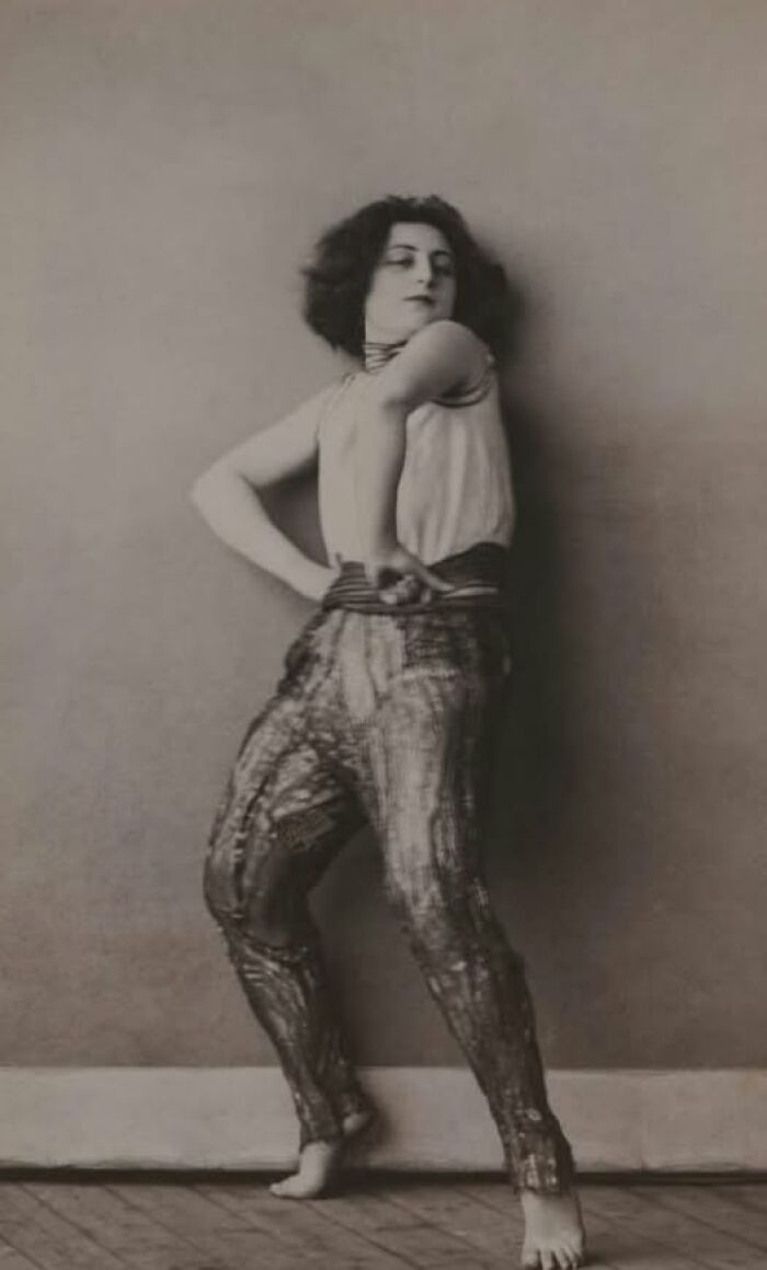 Vintage dancer posing barefoot against a wall, showcasing timeless fashion from over a hundred years ago.